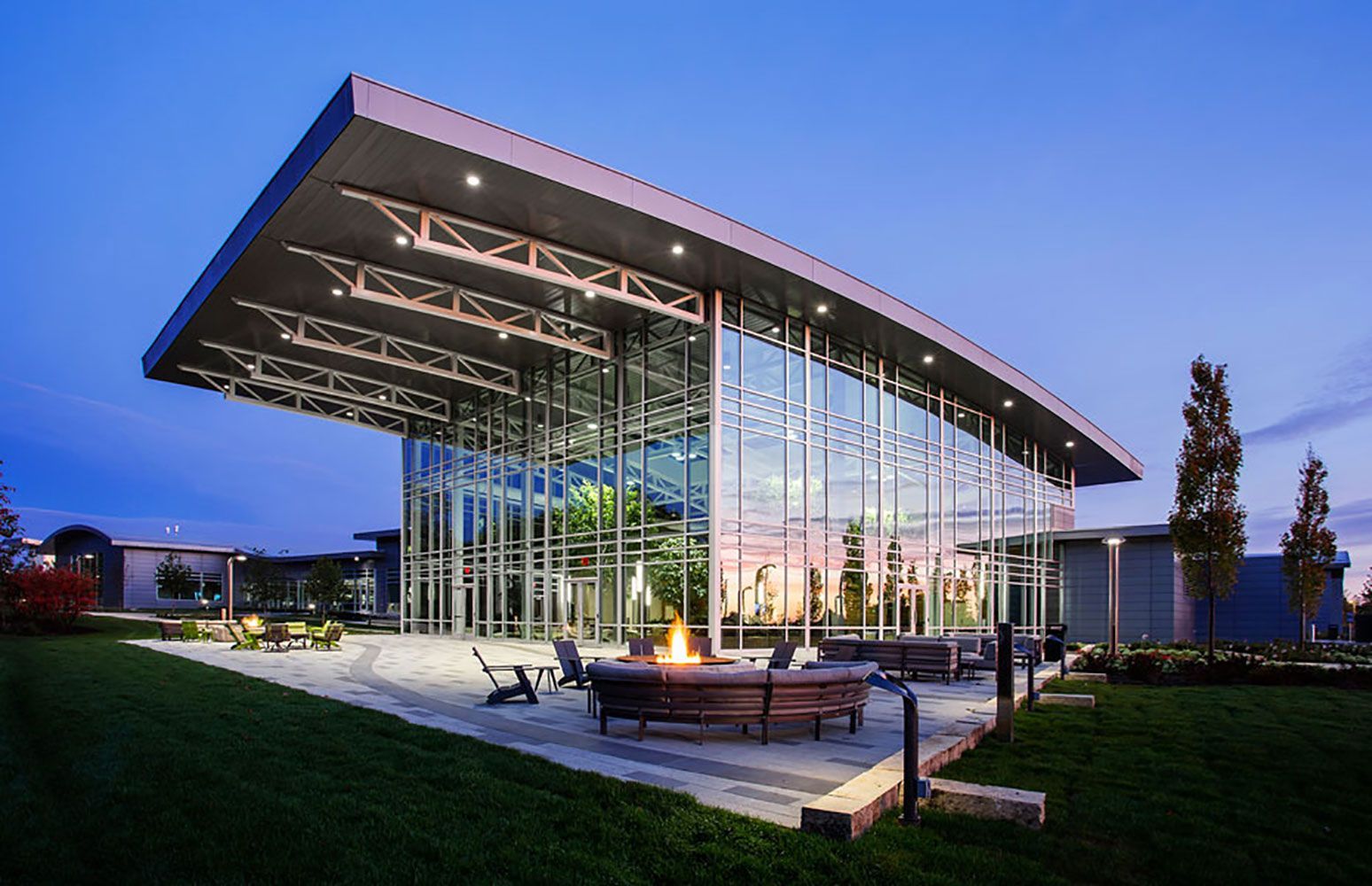 Modern glass building with a dramatic cantilevered roof at dusk, a lit courtyard, and a reflective facade