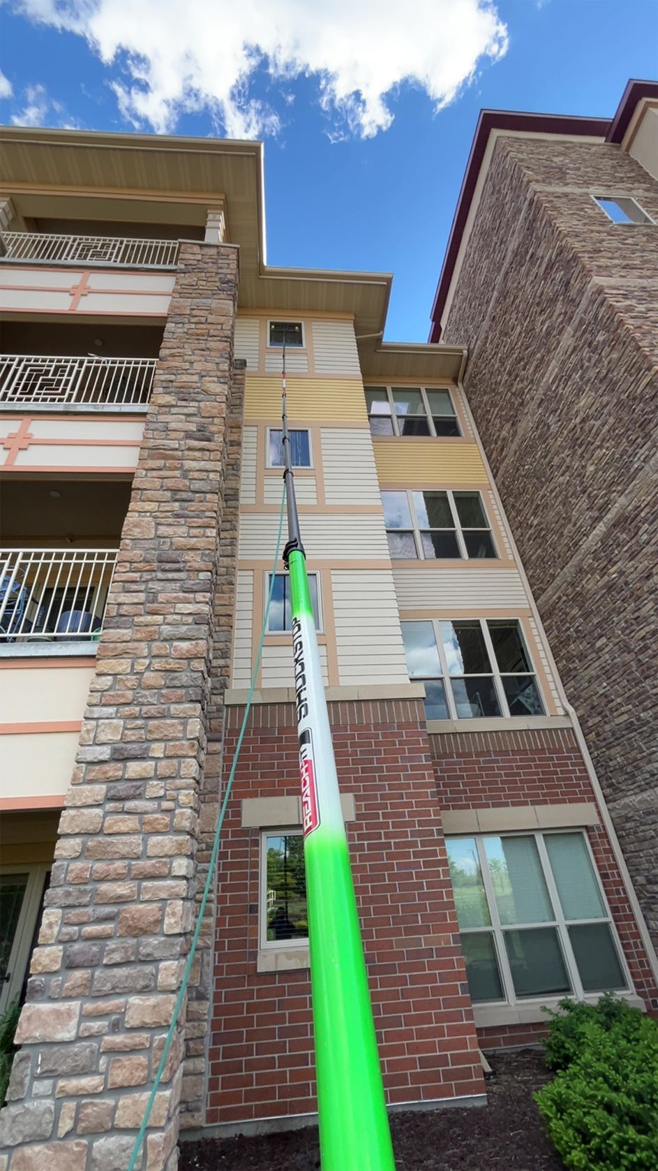 Low-angle view of a brick apartment building with balconies and a green pole against a blue sky