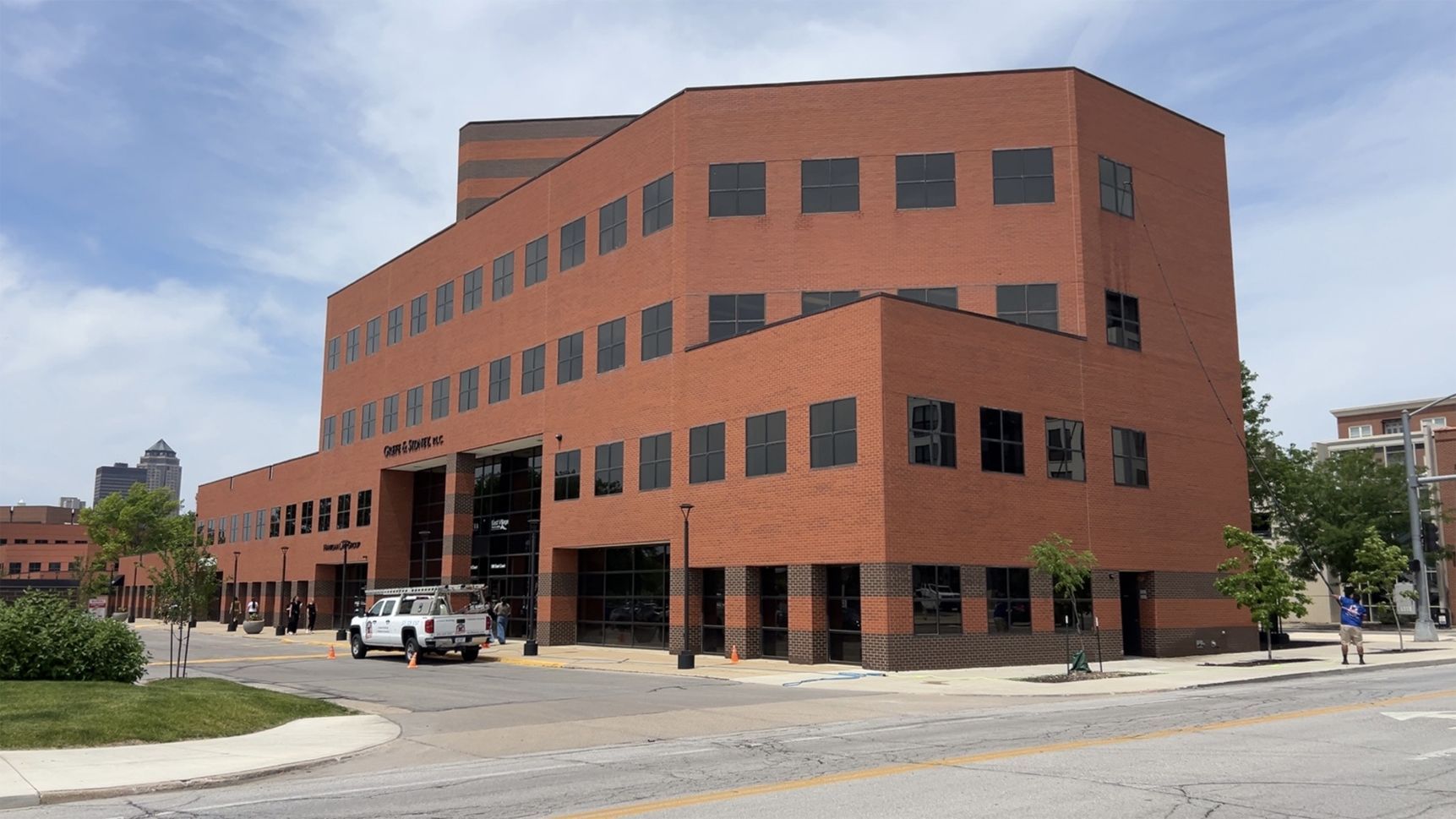 Red-brick office building on a street corner with parked cars and cloudy sky