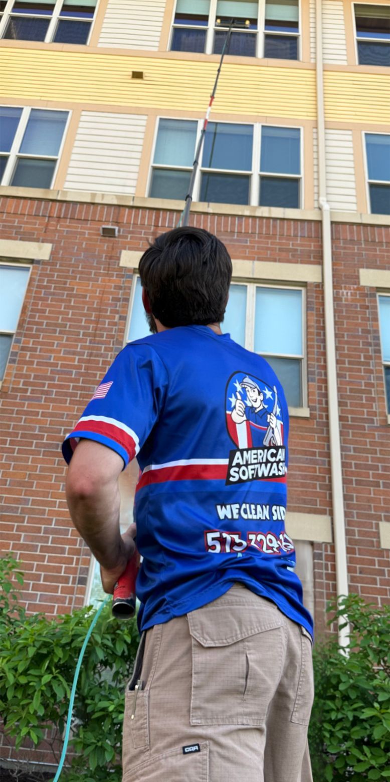 A person in a blue shirt stands looking up at a brick apartment building with windows.