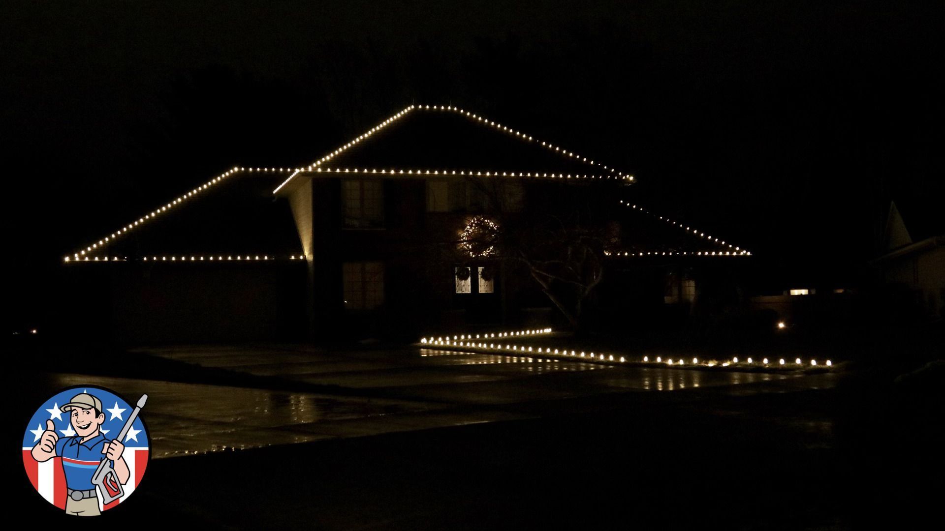 A house at night outlined with white string lights, with a small illuminated decoration in the front yard.