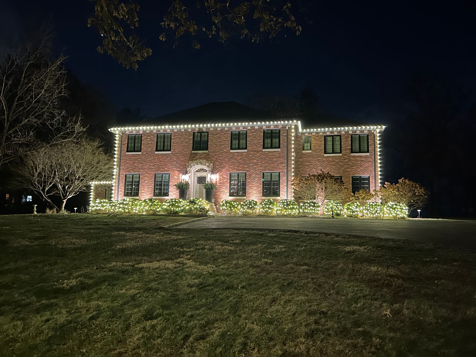 Illuminated brick house at night on a grassy lawn, with lit windows and a dark sky