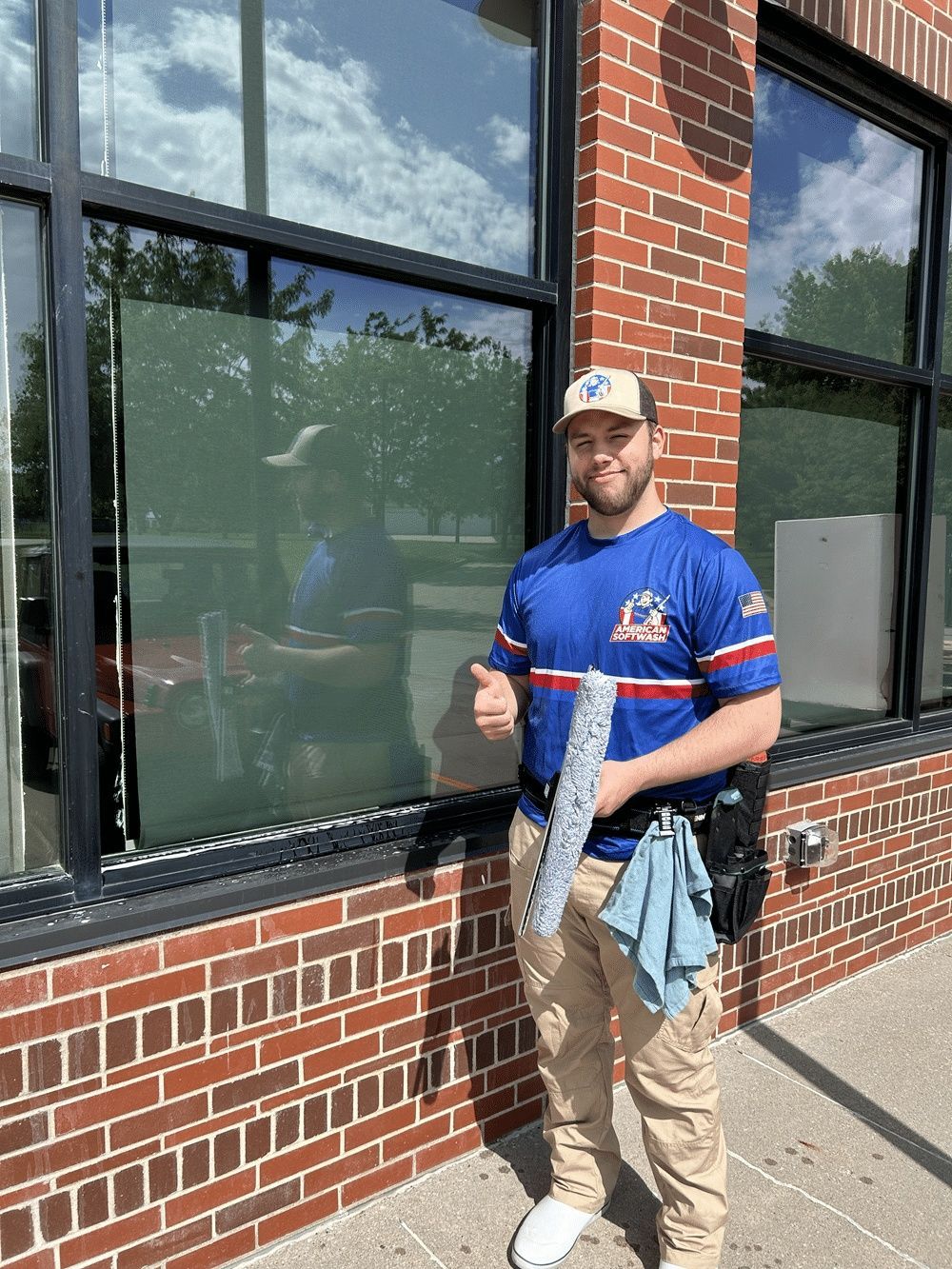 Man in blue shirt and tan pants holding a fish, standing outside a brick building with large windows.