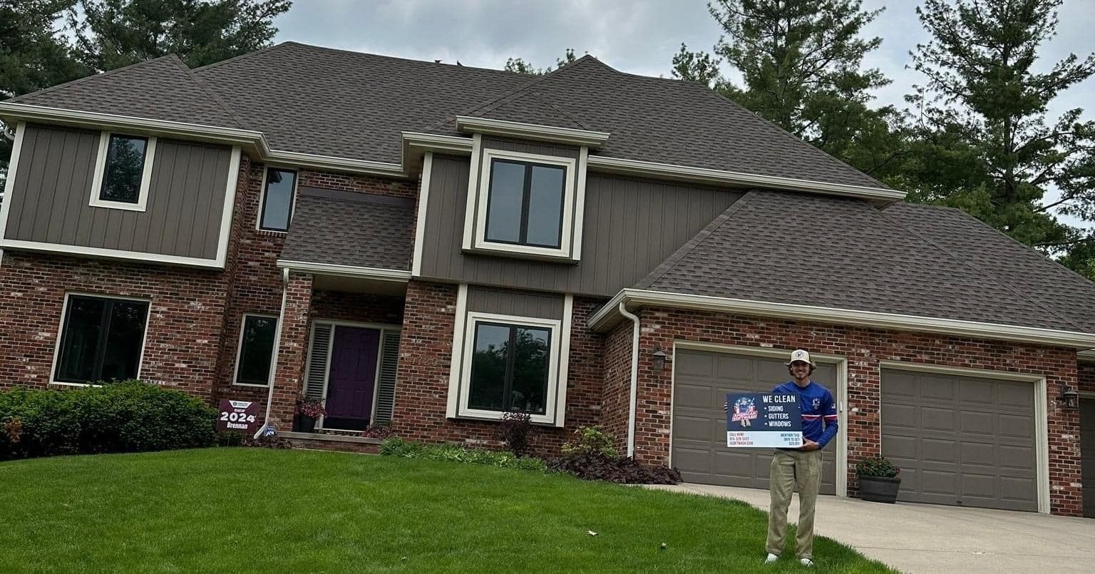 Two-story brick-and-siding house with a driveway and a person holding a real estate sign in the front yard