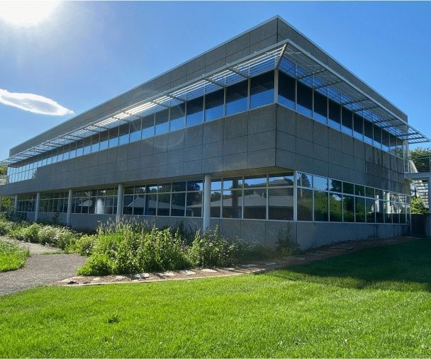 Modern glass-and-metal office building with a slanted roof, surrounded by green lawn under a clear blue sky