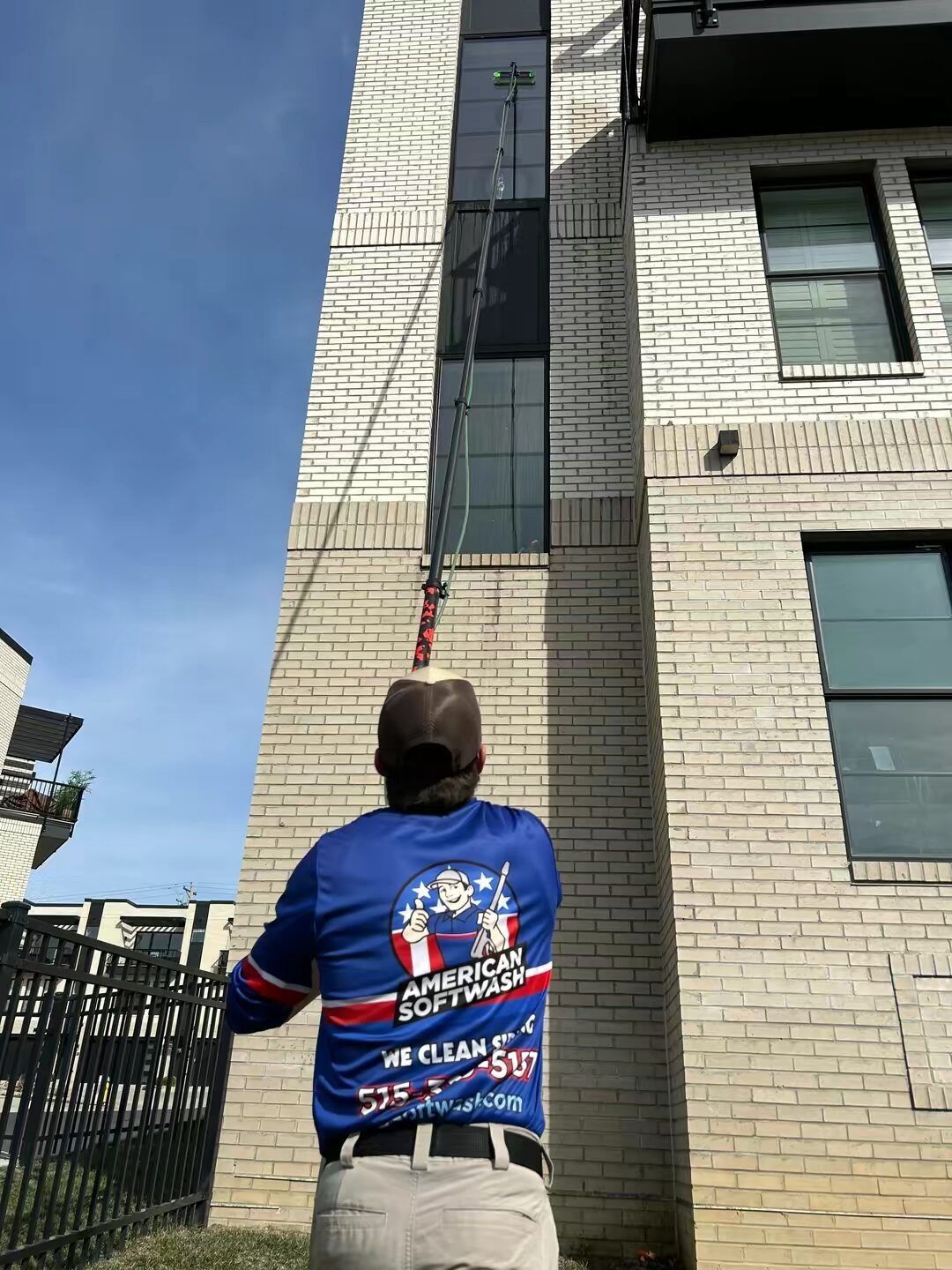 Person in blue jacket hanging from a rope against a tall brick building under a blue sky
