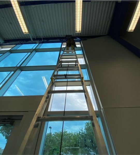Tall ladder leaning up to a high indoor window near a ceiling in a large industrial room
