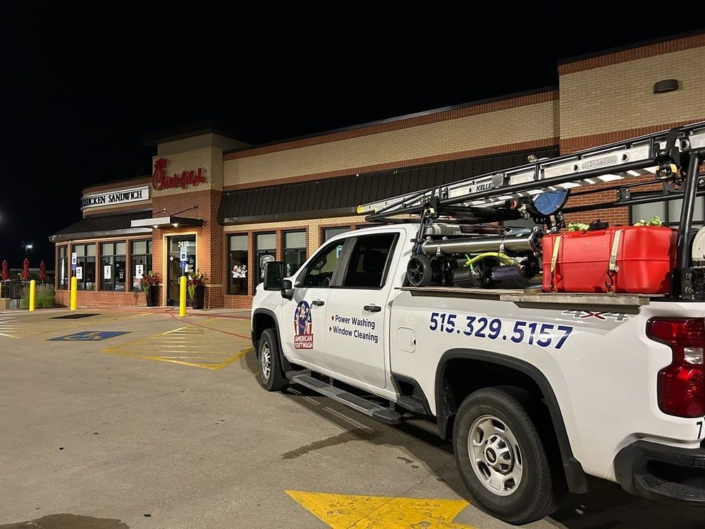 White utility truck parked outside a storefront at night, with ladder rack and red equipment on back.