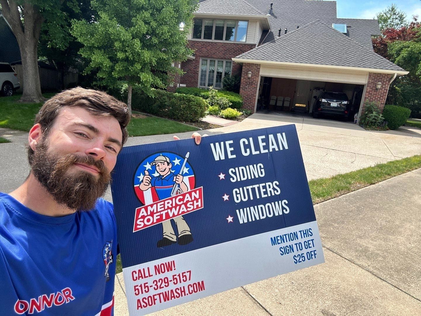 Man holding a sign for American Softwash in front of a brick house and driveway.