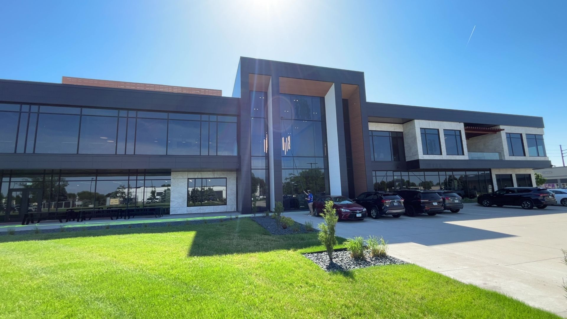 Modern office building with a glass entrance, dark windows, and a bright green lawn in front