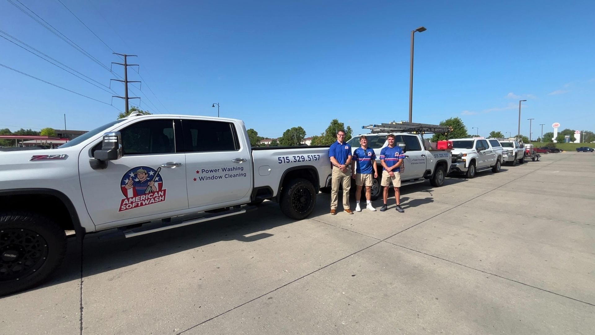 Parade vehicles lined up on a sunny street, with people standing beside a white pickup truck.