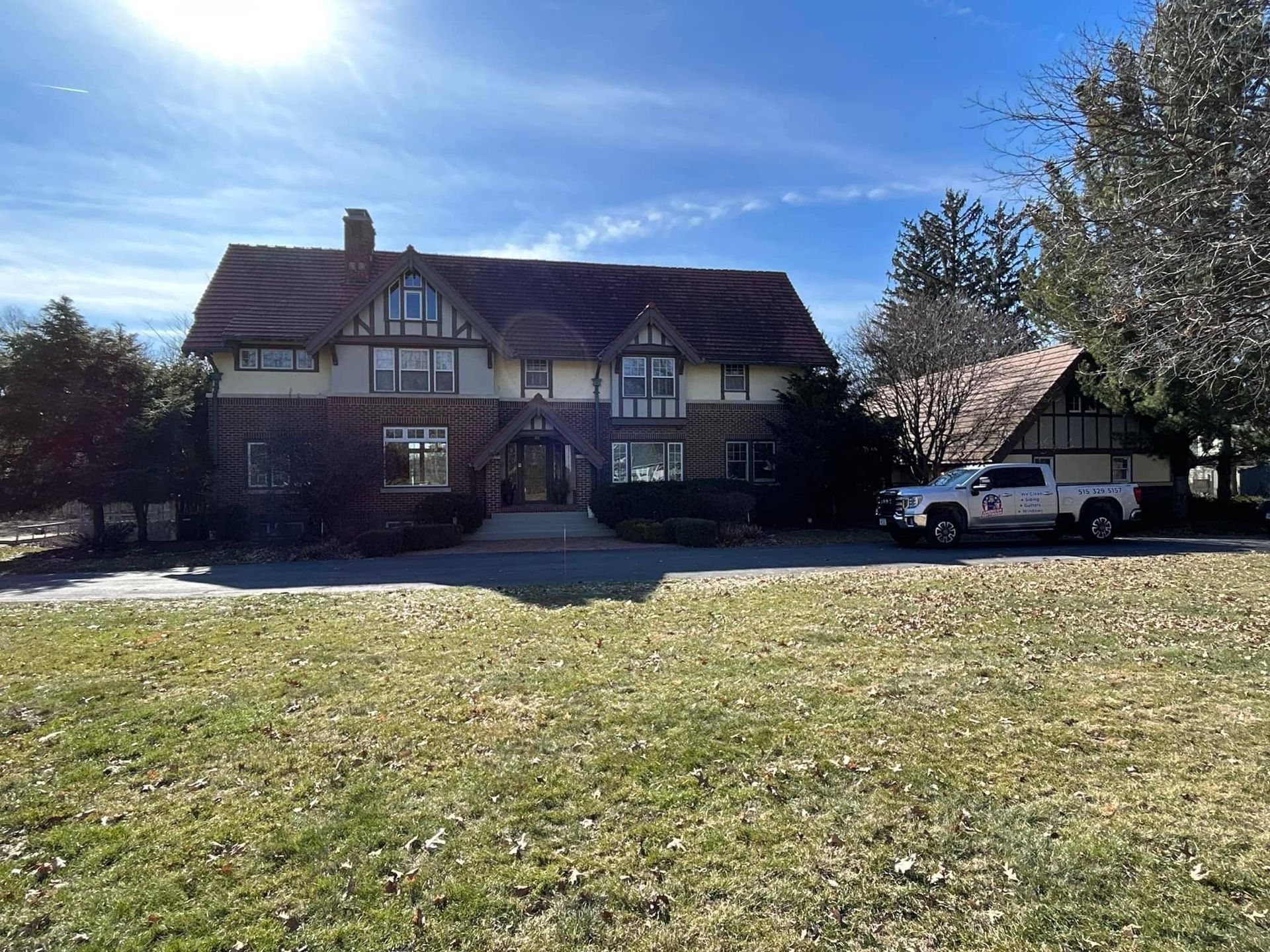 Large Tudor-style house with a red roof, front lawn, and a white car parked in the driveway.