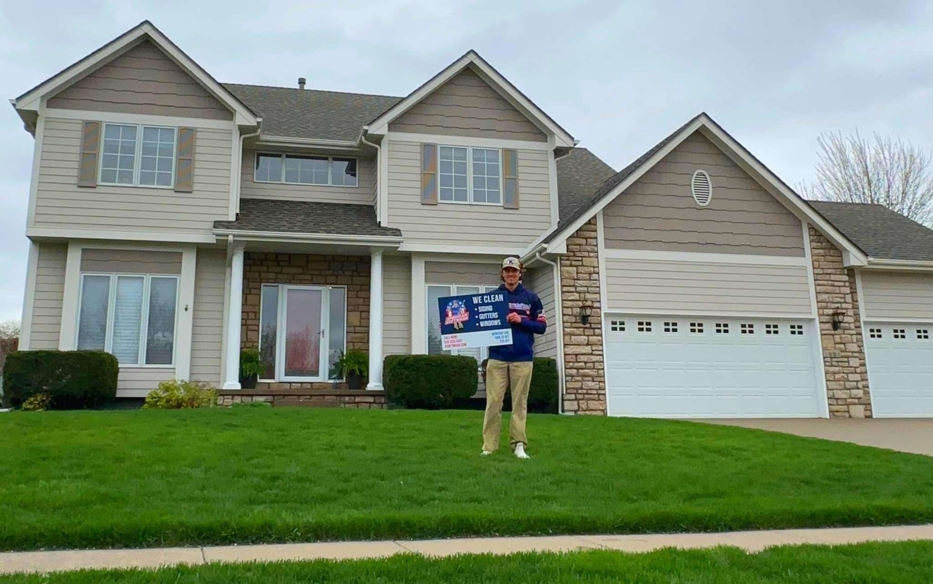 Person holding a campaign sign stands on a lawn in front of a two-story suburban house.
