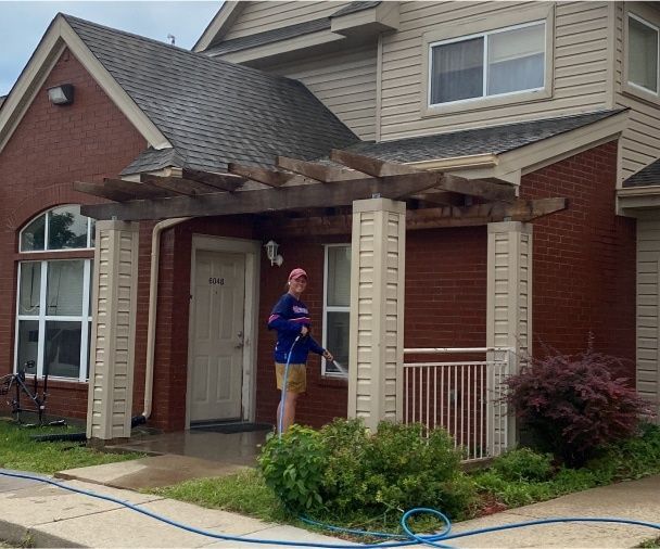 Person washing a house’s front porch and columns with a pressure washer