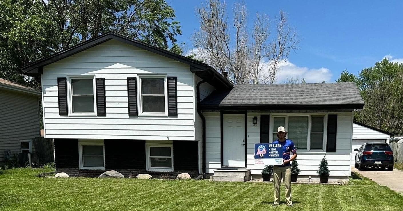 Suburban house with a person holding a sign in the front yard and a car in the driveway.