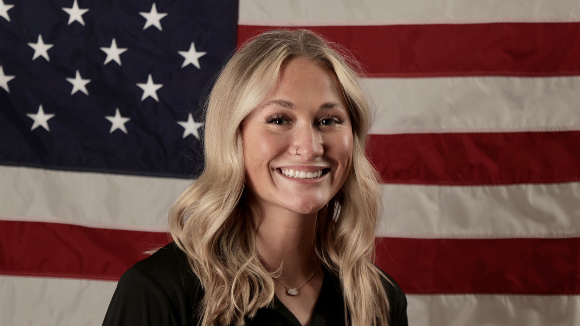 Smiling person in front of a large American flag backdrop