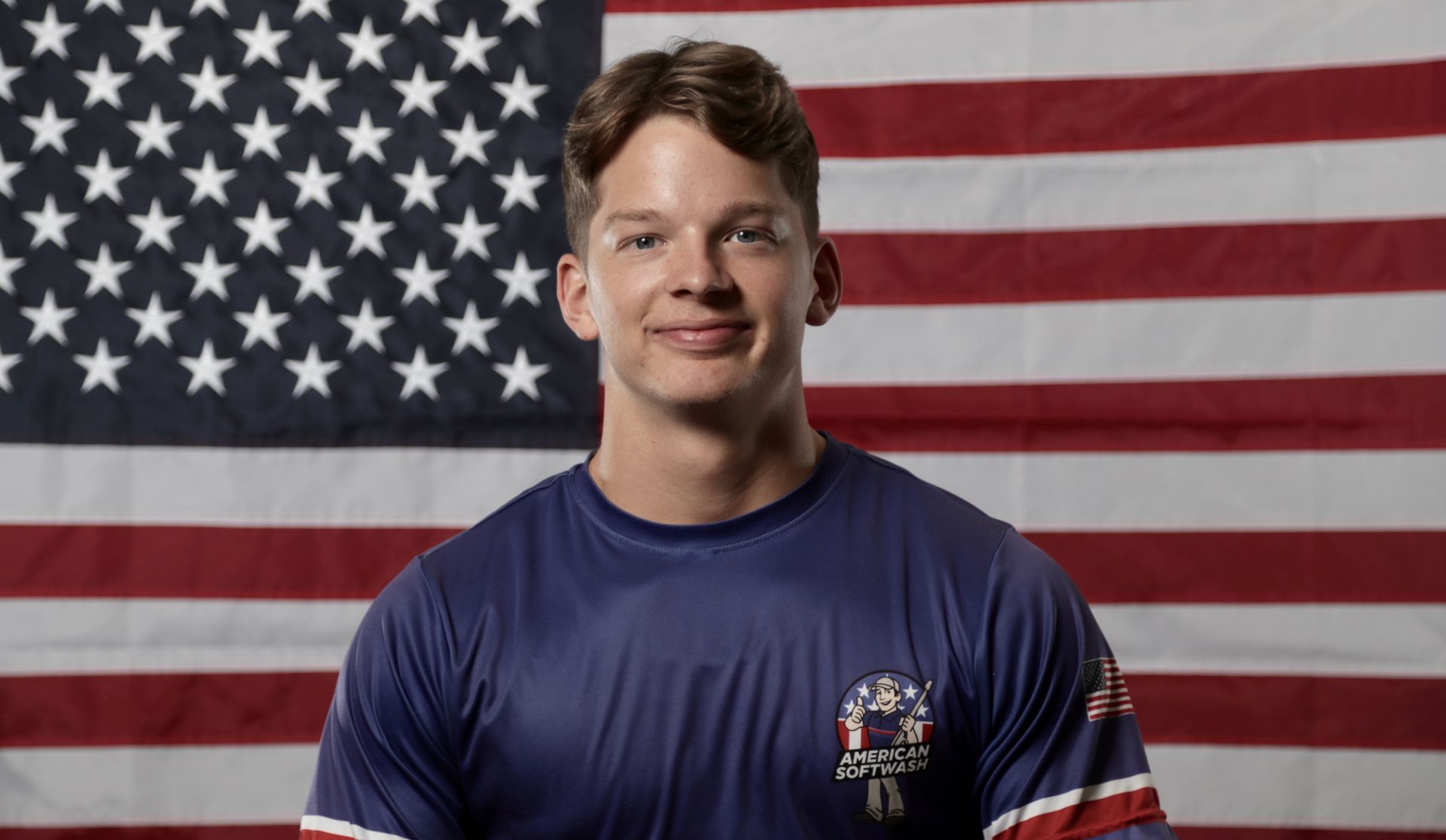 Man in a navy shirt standing in front of a large American flag backdrop
