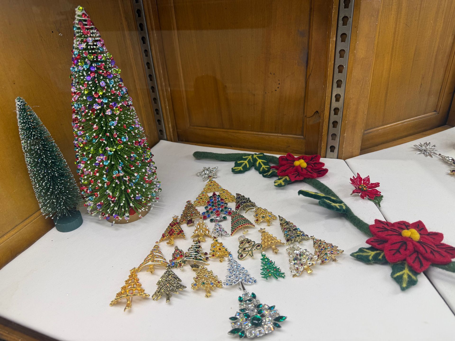 Christmas-themed display with multiple brooches arranged as a Christmas tree, alongside bottle-brush trees and poinsettia decorations.