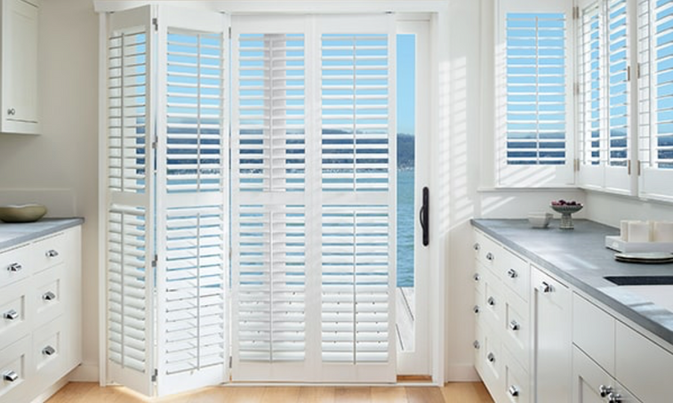 A kitchen with white cabinets and shutters on a sliding glass door.