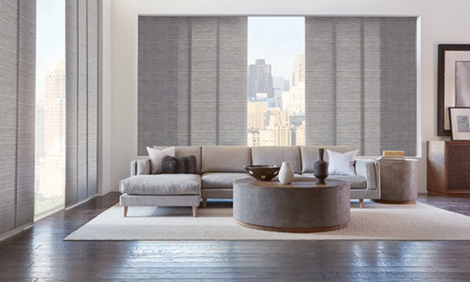 A living room with a couch , coffee table , and sliding panel blinds.