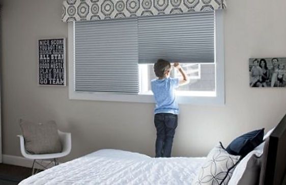 A young boy is looking out of a window in a bedroom.