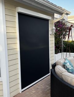 A patio with a couch and a black screen door on the side of a house