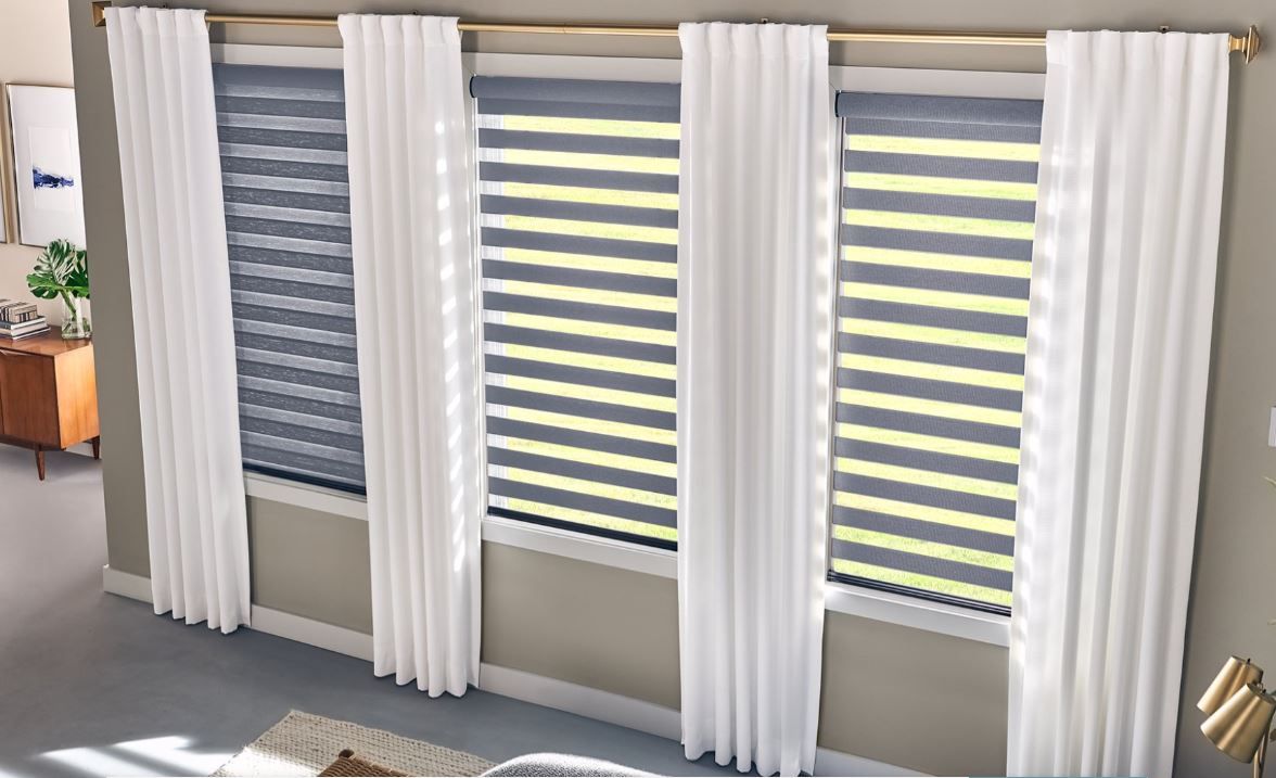 Three windows with gray blinds and white curtains in a well-lit room