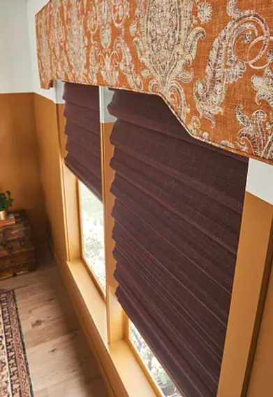 A pair of brown roman shades on a window in a room.