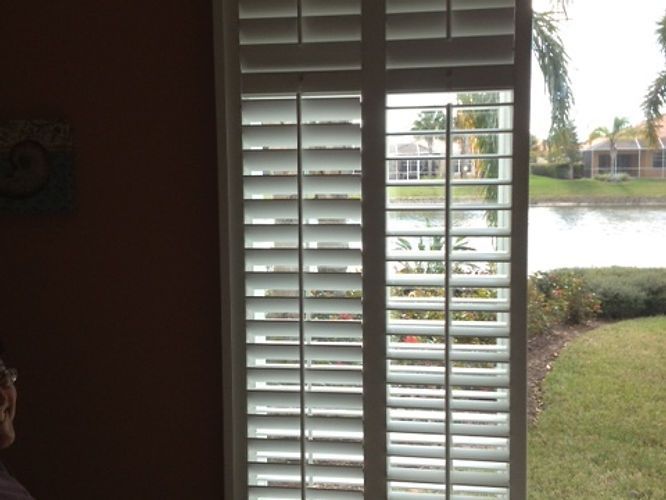 A person is looking out of a window with shutters on it.