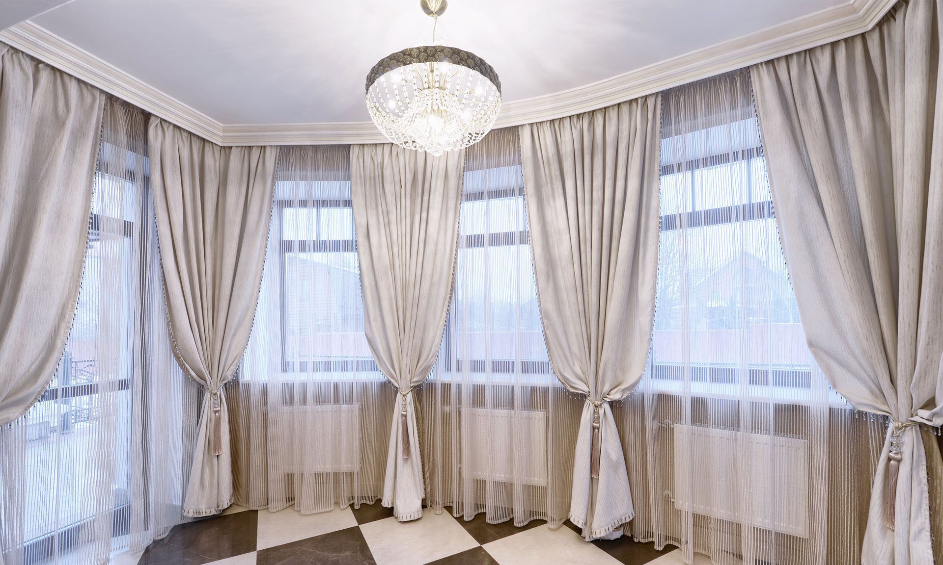 A room with a lot of windows and curtains and a chandelier.