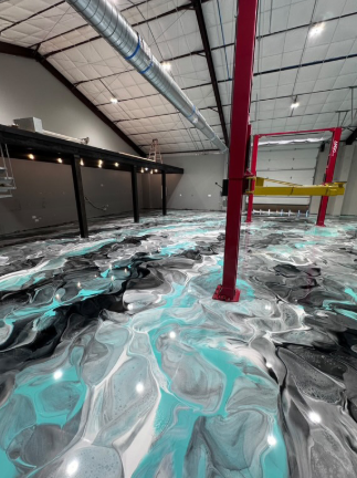 Epoxy flooring in turquoise, black, and white flows through a large, industrial-style room with red beams.