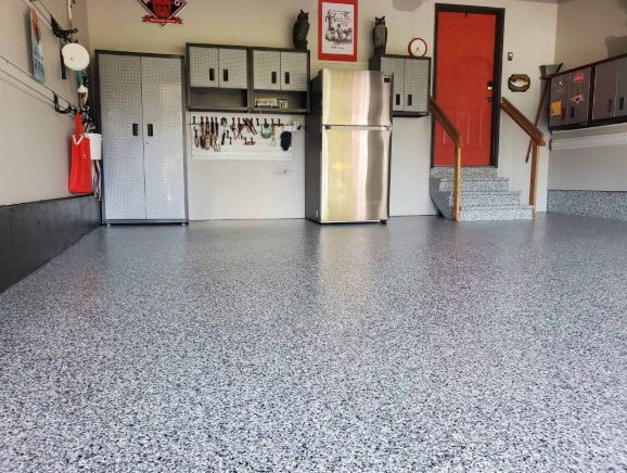 Garage interior with gray epoxy floor, cabinets, refrigerator, and red door.
