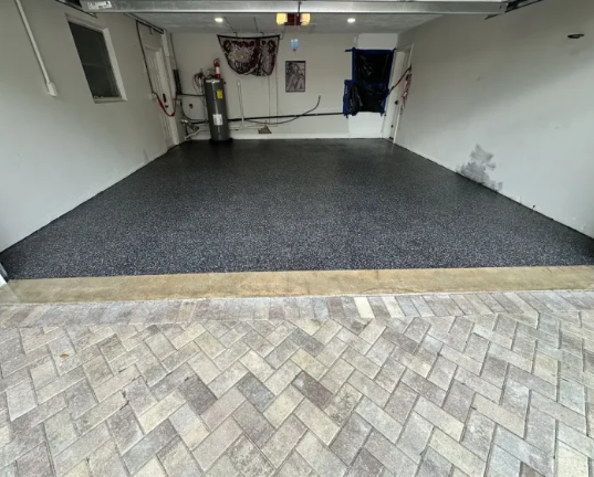 Garage with a black speckled floor and light gray herringbone brick entrance.