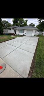 Concrete driveway leading to a white house with a garage and front yard.