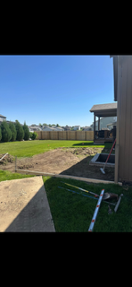 Backyard with green lawn, patio, and house exterior under a clear blue sky