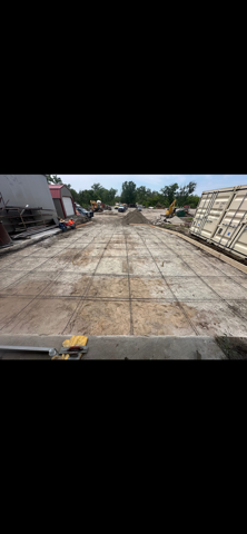 Empty concrete lot with construction materials and equipment along the sides under a clear sky