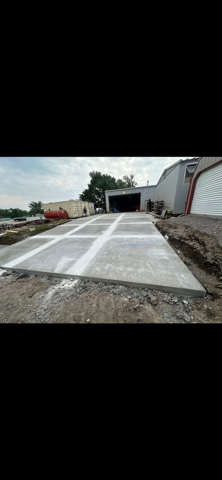 Concrete driveway ramp under construction beside buildings, with fresh white lane markings and gravel edges