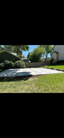 Sunny backyard patio with white pavers, green grass, and trees beside a house