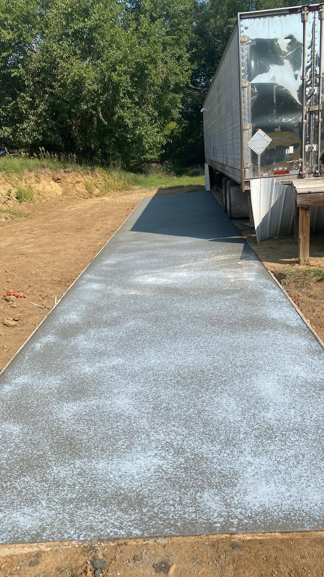 A semi truck is parked on the side of a concrete driveway.