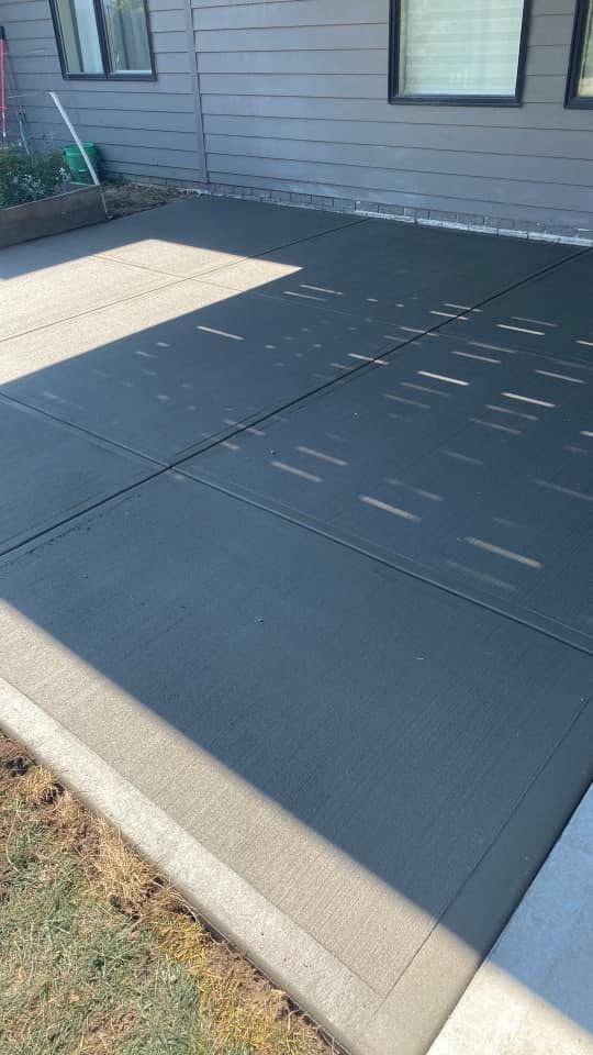 A black concrete driveway with a house in the background.
