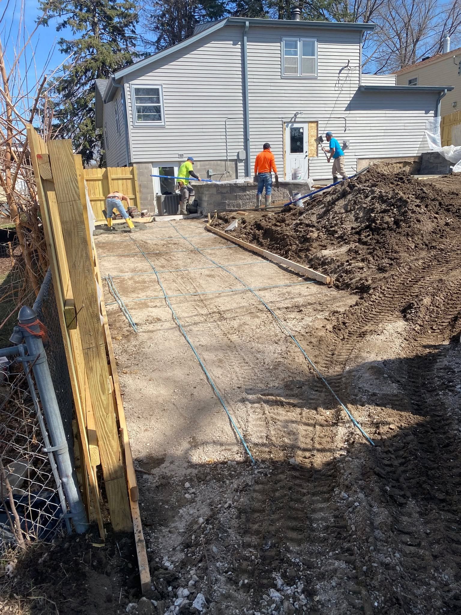 A group of construction workers are working on a driveway in front of a house.