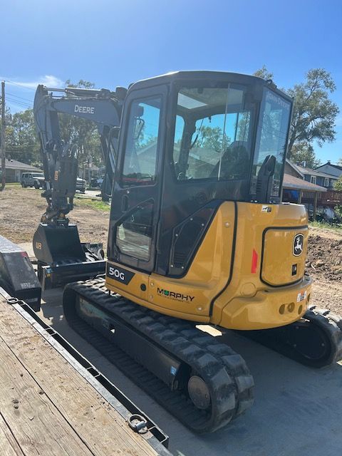 A small yellow excavator is parked on a wooden deck