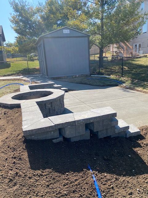 A concrete patio with a fire pit and a shed in the background.