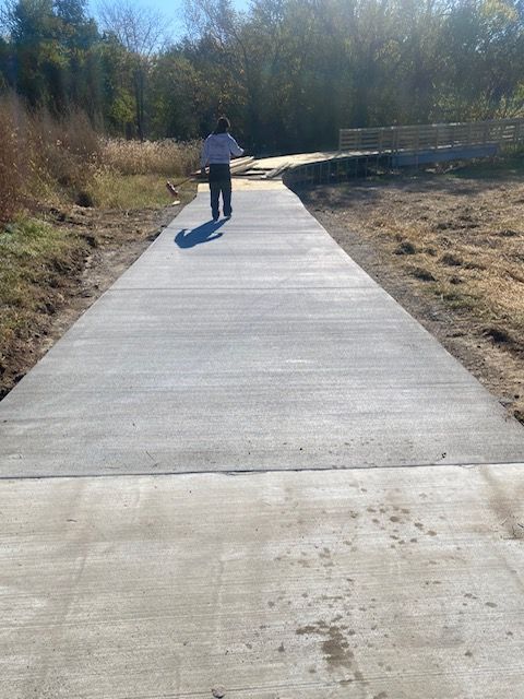A person is walking down a concrete path in the woods.