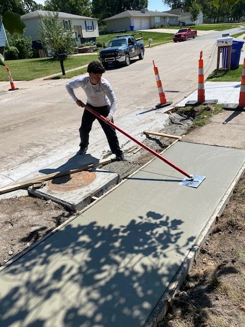 A boy is standing on a sidewalk with a mop.