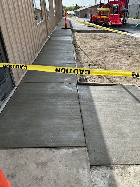 A sidewalk is being built next to a building with a yellow caution tape.