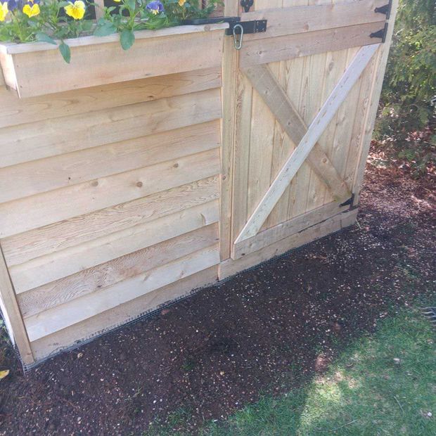 Wooden garden fence with a diagonal-braced gate beside a dirt path and plants on top