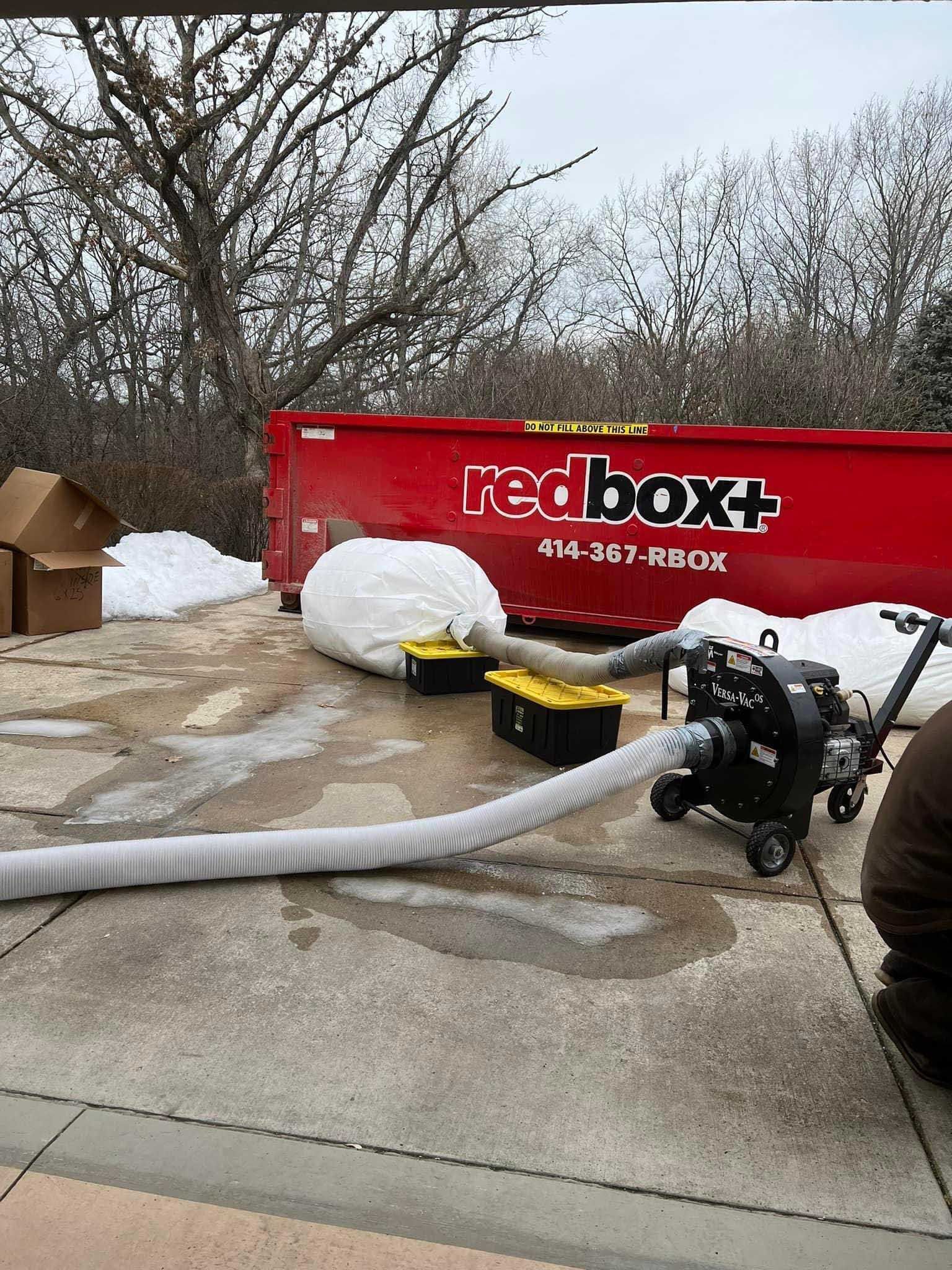 Worker pumps liquid into a red box truck using a hose outdoors in a snowy lot