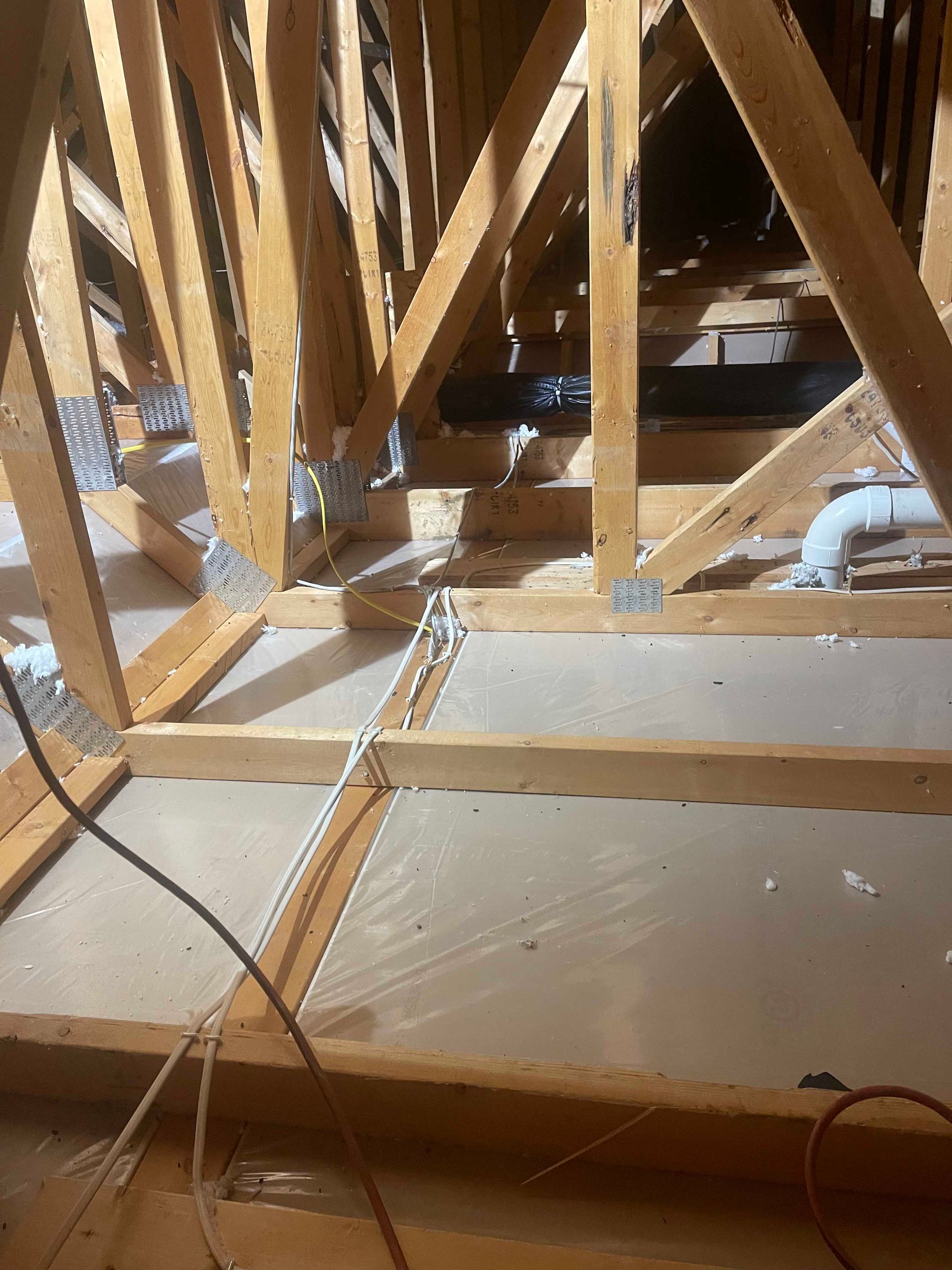 Exposed attic framing with wooden beams and roof trusses over an unfinished floor, with cables in foreground