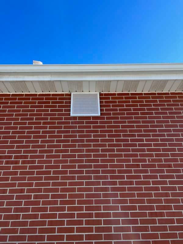 Red brick wall of a building with a white roof overhang and small white vent against a blue sky